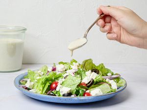 A spoon drizzling dressing onto a green salad with various toppings on a plate