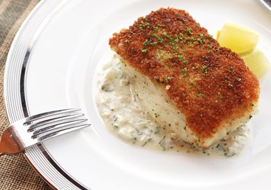 A piece of pan-seared fish with a crispy crumb coating on top, sprinkled with chopped herbs. 