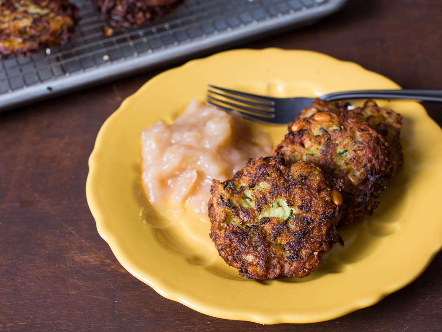 A yellow plate of zucchini-Parmesan latkes with applesauce