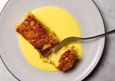 A slice of torrijas caramelizadas, Spanish-style caramelized custard-soaked toast, on a plate served with crème anglaise. 