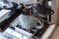 A cup placed under an espresso machine spout, with liquid coffee being dispensed into it on top of Acaia Lunar Scale