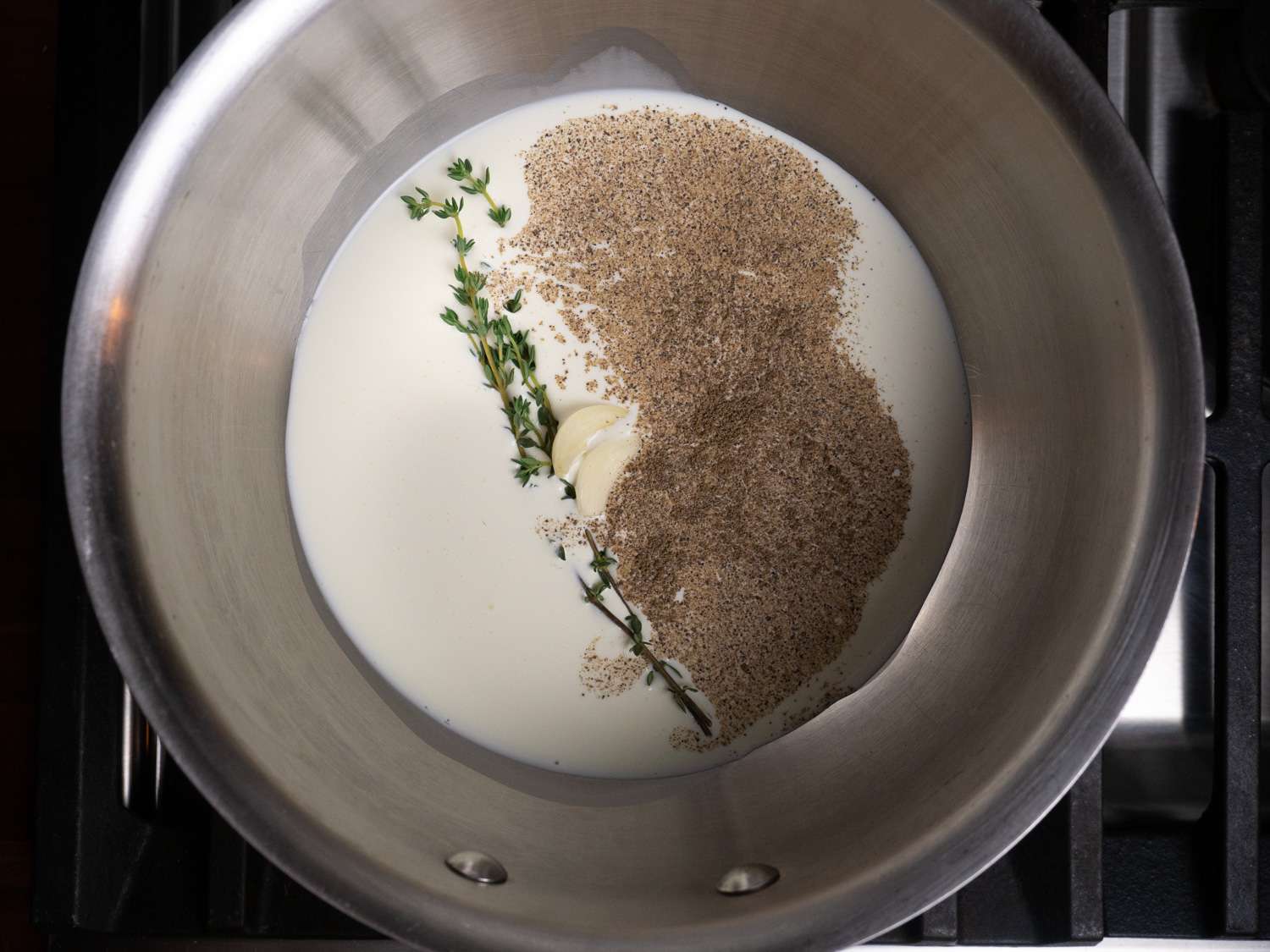 Overhead view of the cream, garlic, thyme, and black pepper in a saucier.