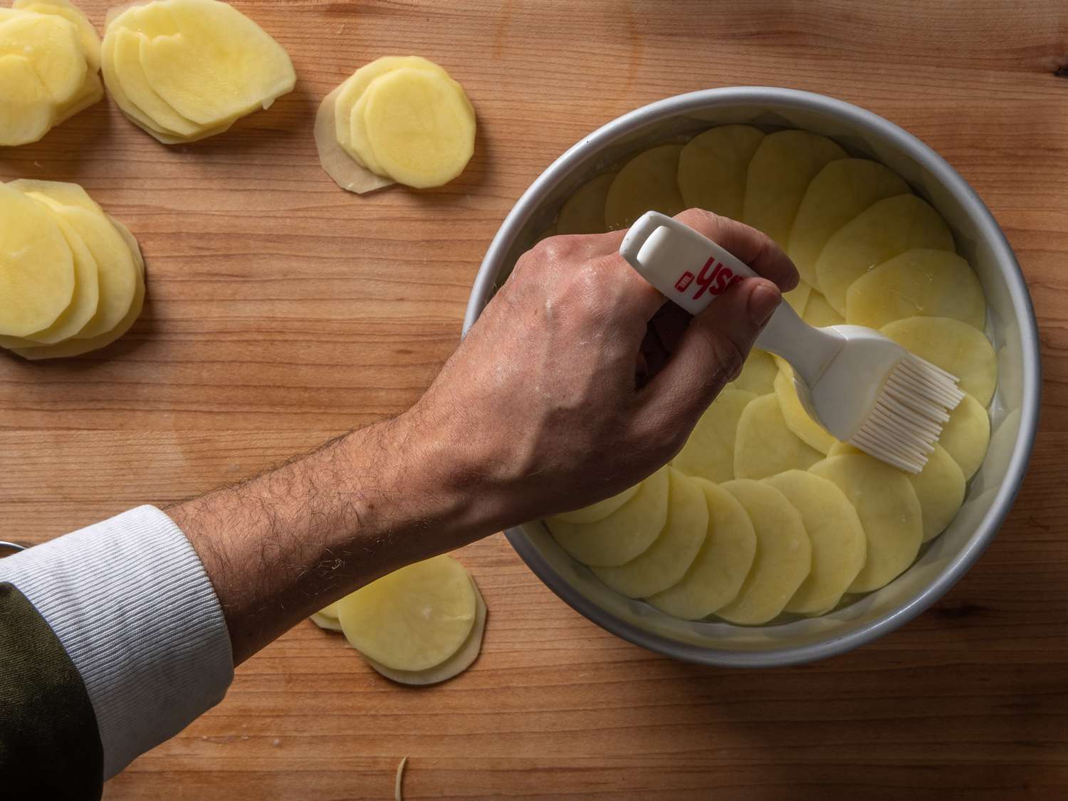 Brushing the shingled potato slices with clarified butter.