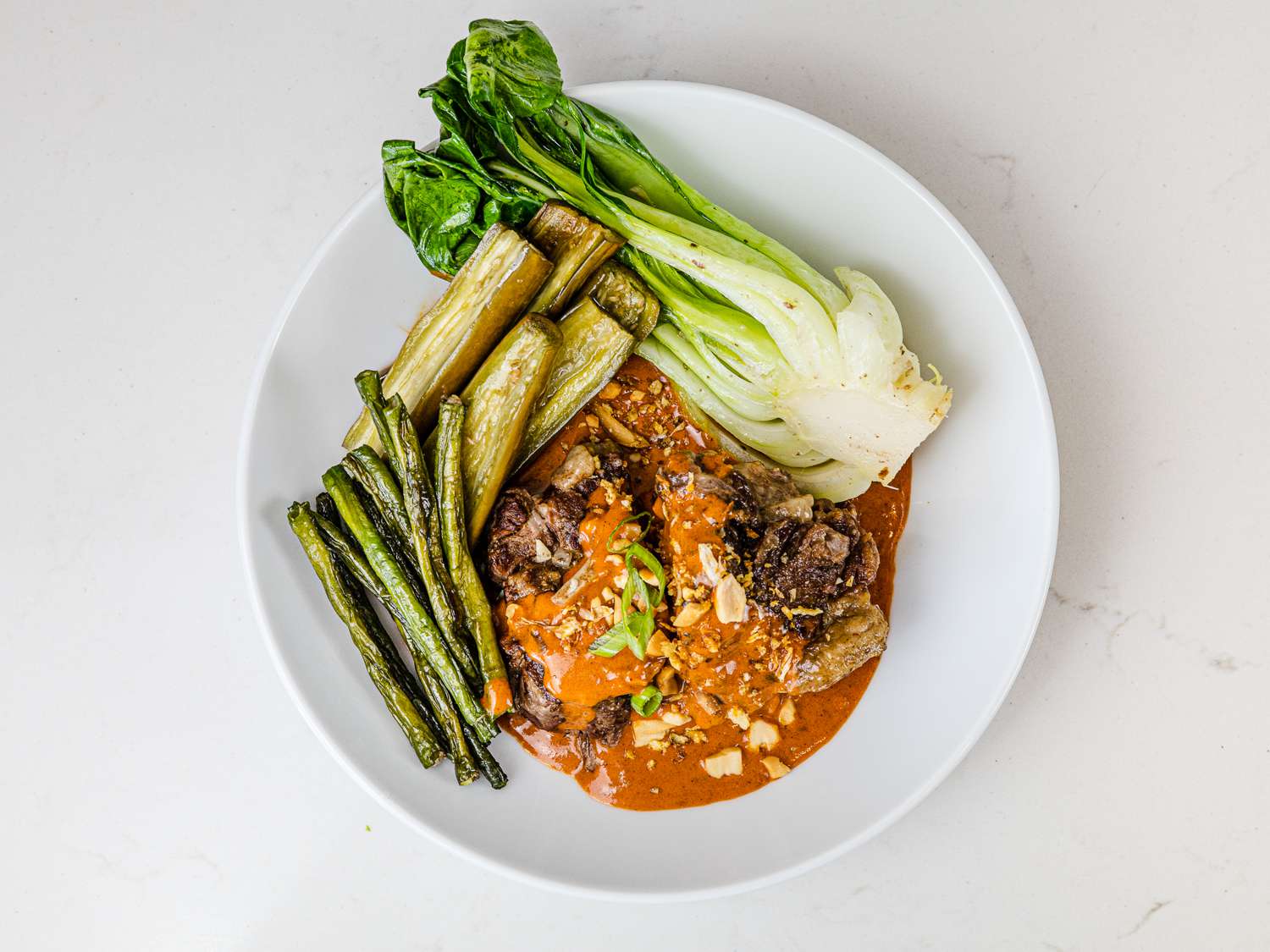 Serving bowl of kare kare with bok choy, oxtails, roasted eggplant and long beans on top