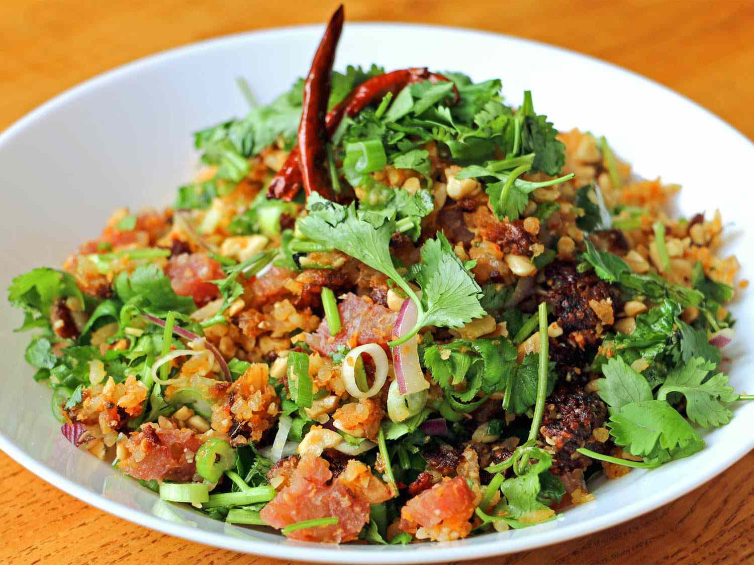 A bowl of crispy coconut rice (naem khao): steamed and dried white rice, dried coconut, ground pork, and pork skin, garnished with fresh herbs.