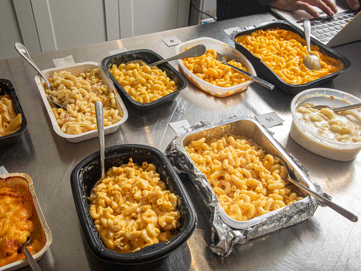 Assortment of mac and cheese dishes on a table with a laptop in the background