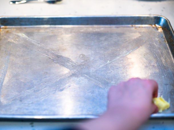 Butter is smeared in an x and along the periphery of a jelly roll pan.