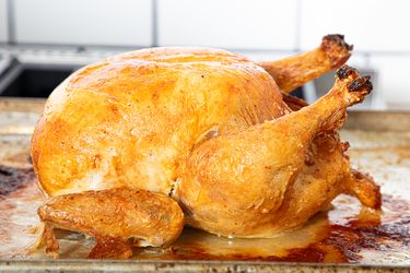 A roasted chicken placed on a baking tray photographed in a kitchen setting