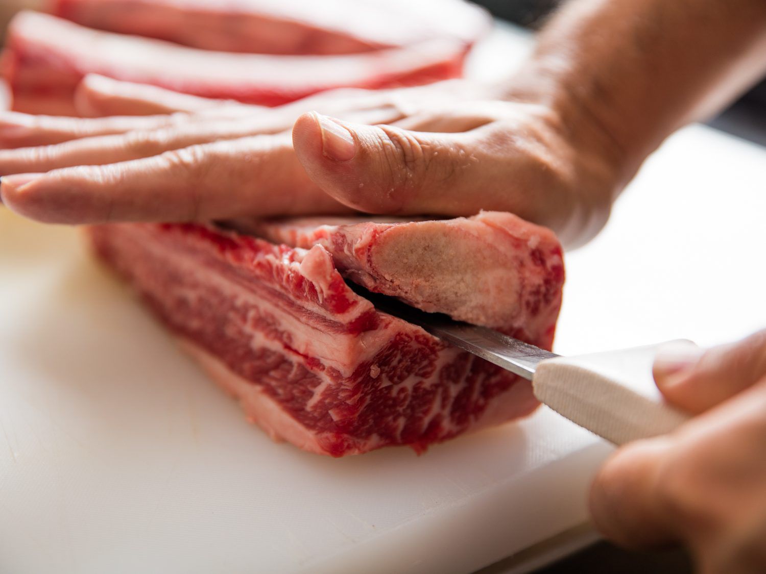 Author deboning a short rib by pressing it against a cutting board, bone-side-up, and slipping a filet knife between the bone and the attached meat.