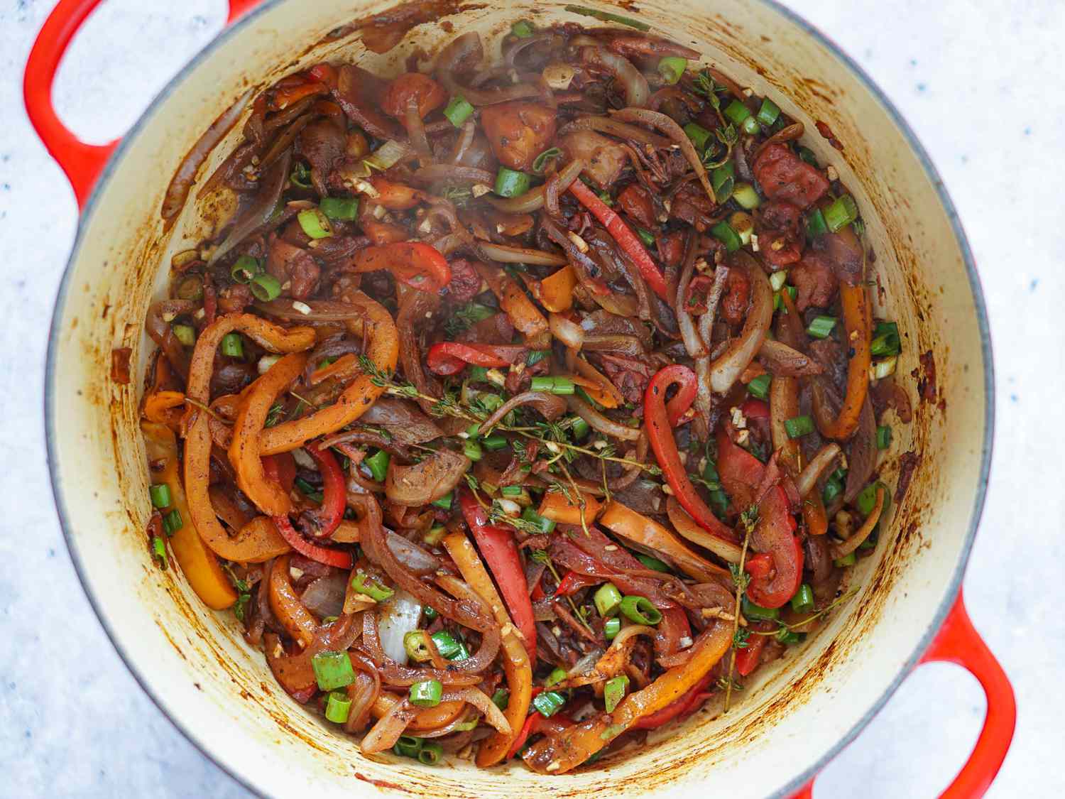 Peppers, onions, scallions, garlic, and thyme being sautÃ©d in a Dutch oven