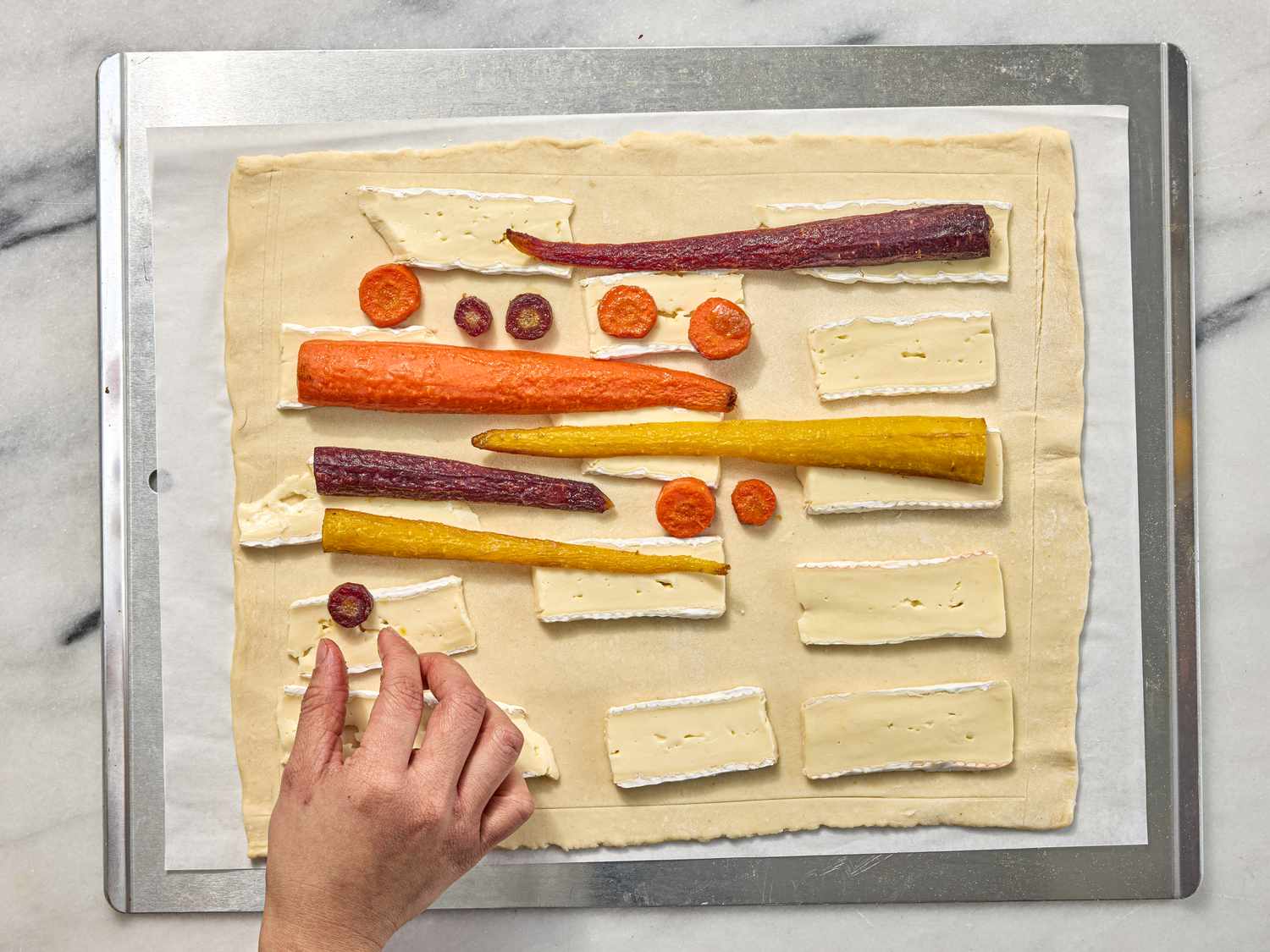 arranging carrots on tart on a sheetpan on a white marble surface 