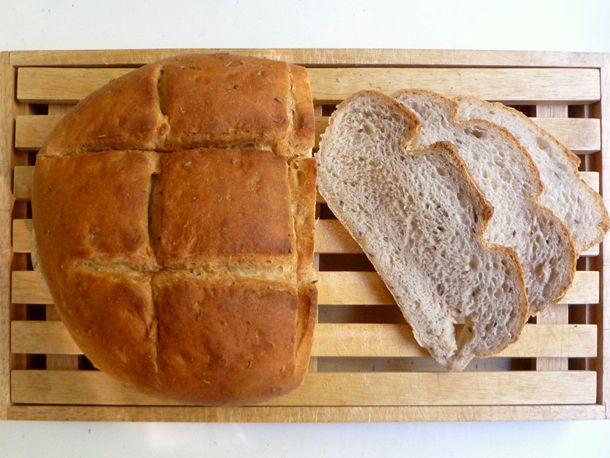 A boule of homemade bread on a wood slat board with three slices next to it. 