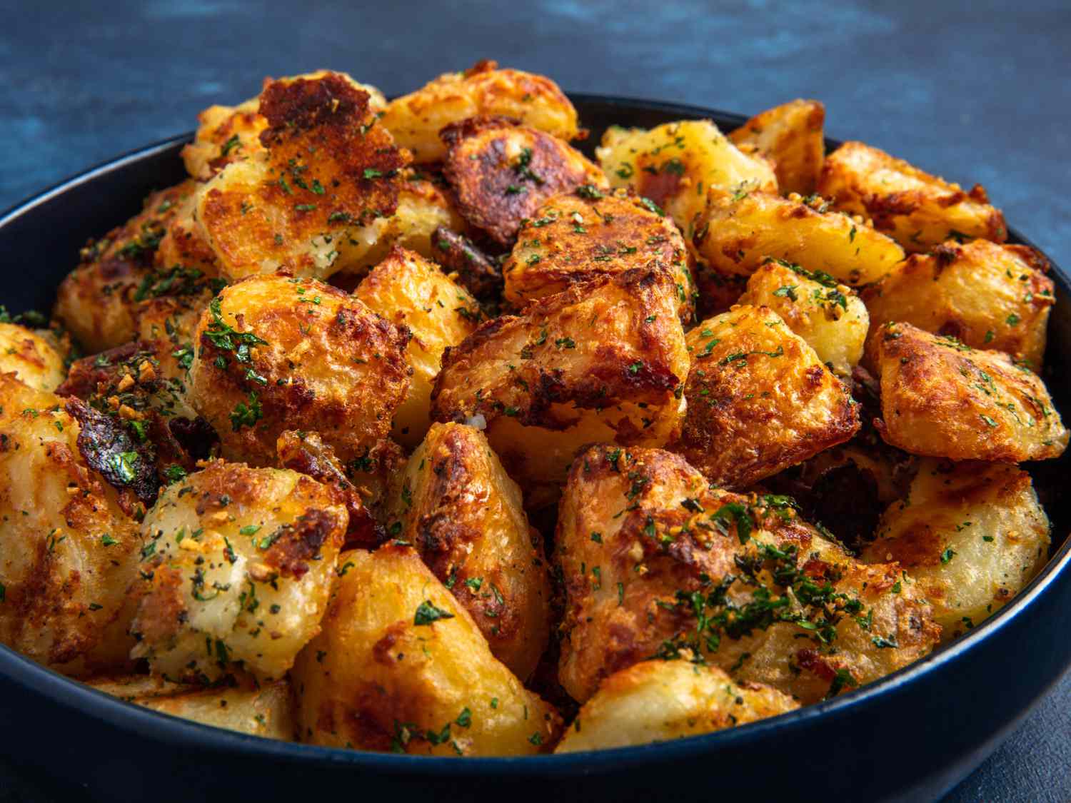 An angled side shot of the crispy roast potatoes in a bowl on a blue background.