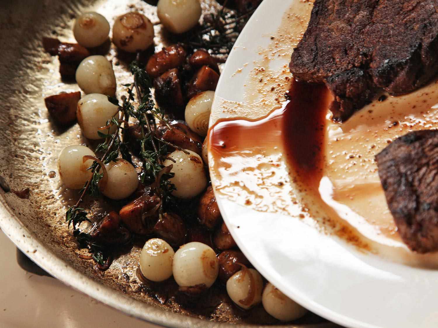 Adding steak juices to a pan of pearl onions, mushrooms, and thyme.