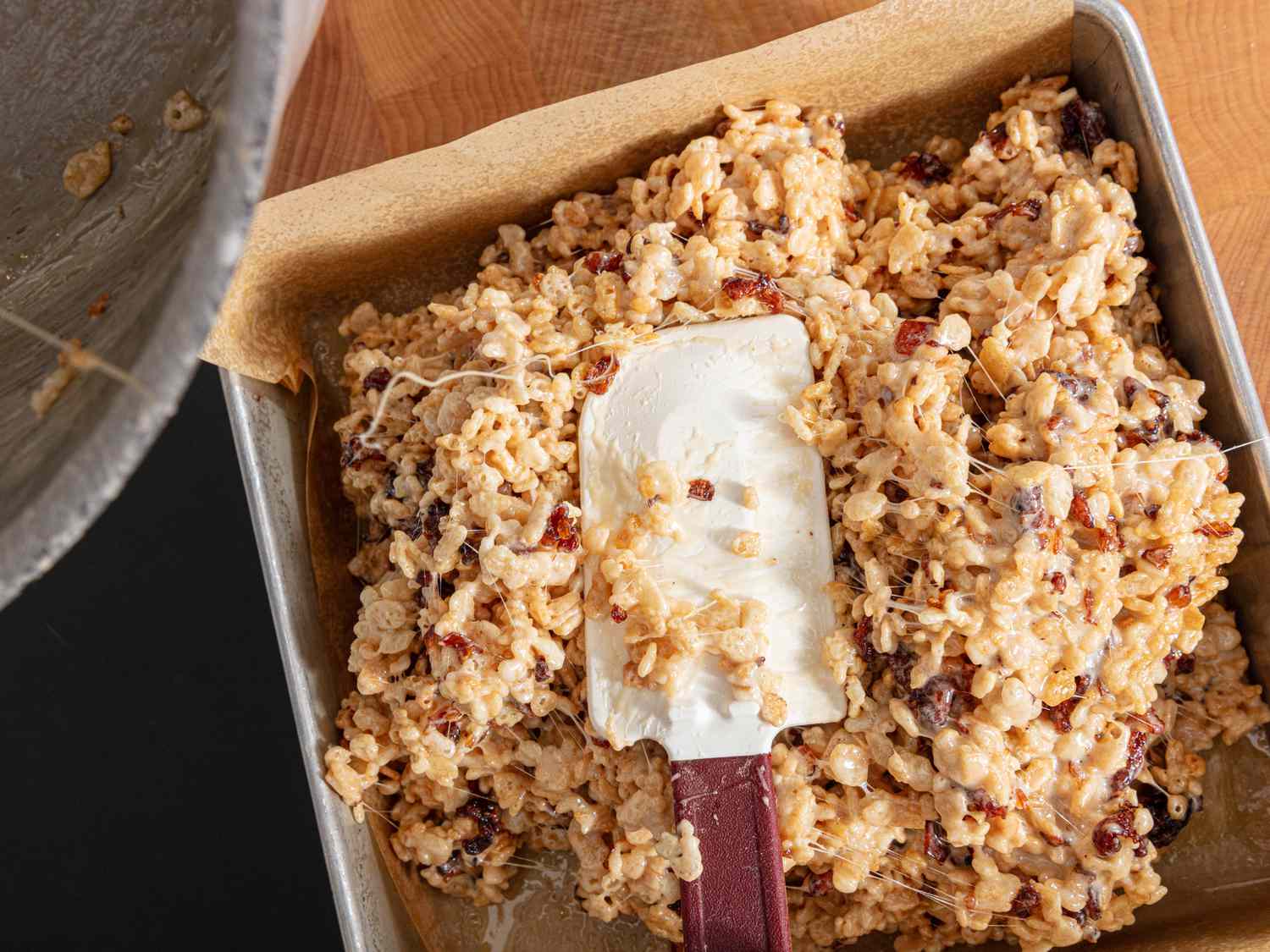 Pressing the rice krispies into a prachment paper lined pan with a silicon spatula