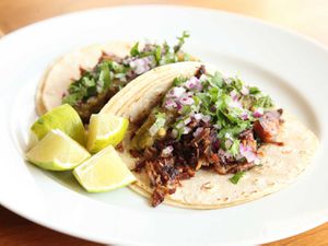 Carnitas tacos on a plate with lime wedges. 