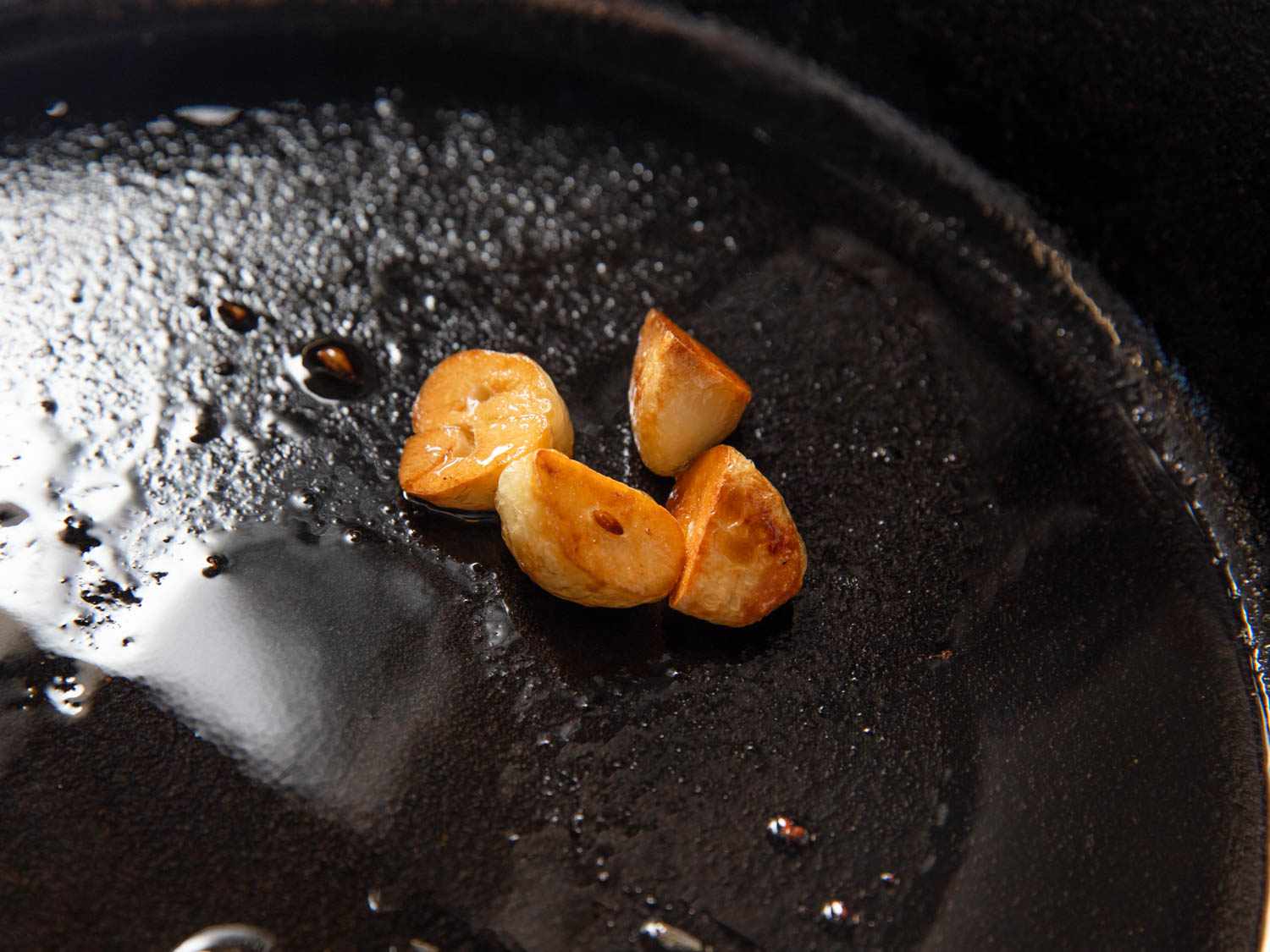 Closeup of halved garlic cloves being browned in a cast iron pan.