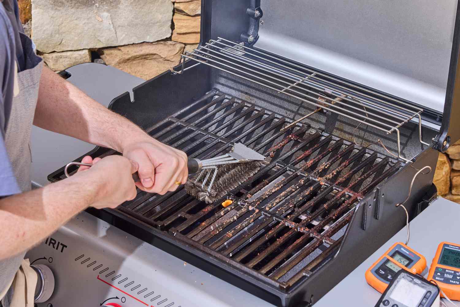 A person using a brush to clean the Weber Spirit E-325 Gas Grill
