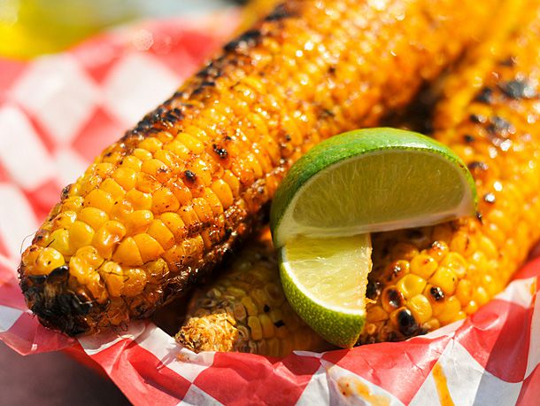 Corn with chile lime butter and lime wedges on a paper plate. 