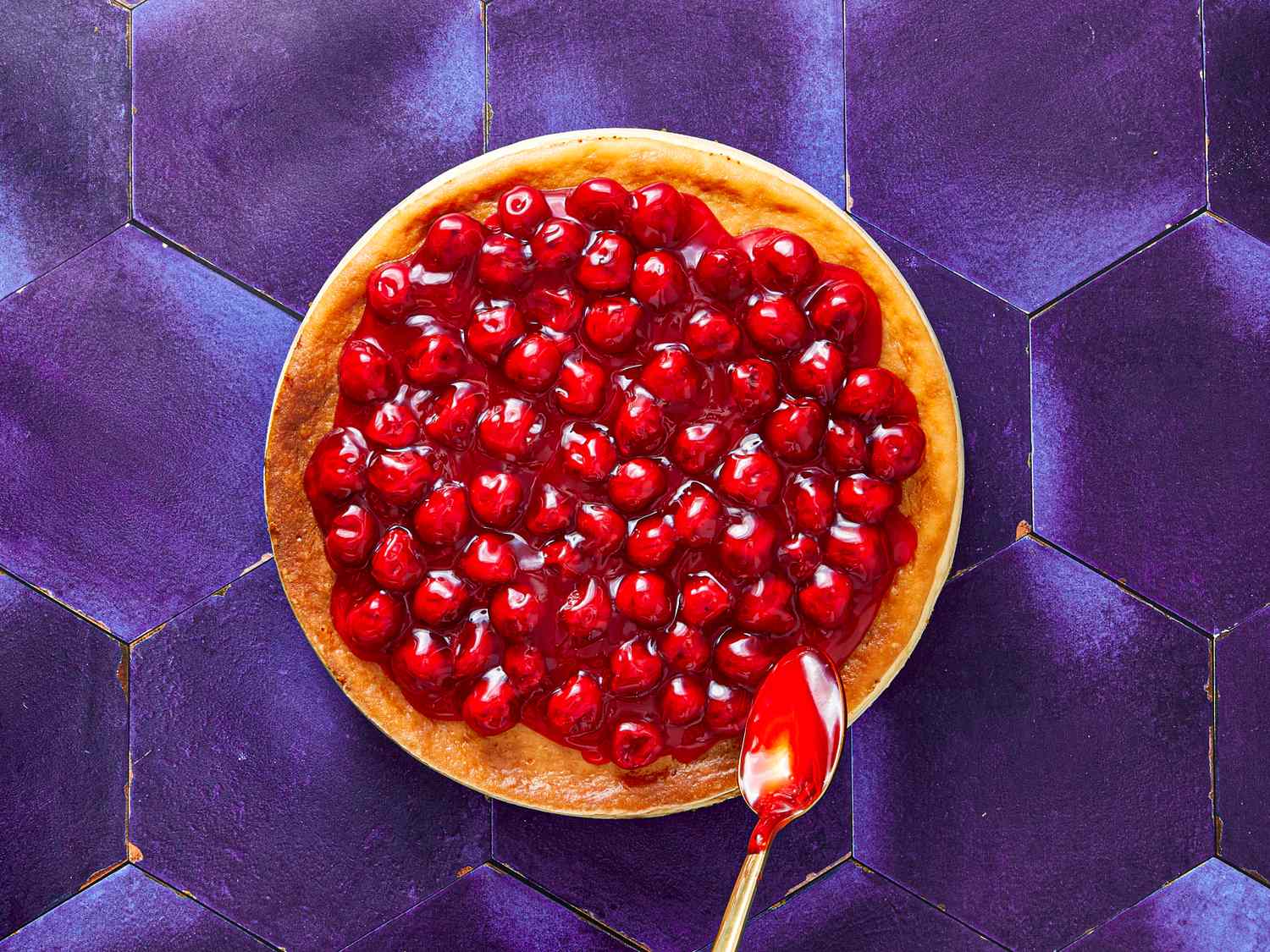A cheesecake topped with cherries set against a hexagonal purple background