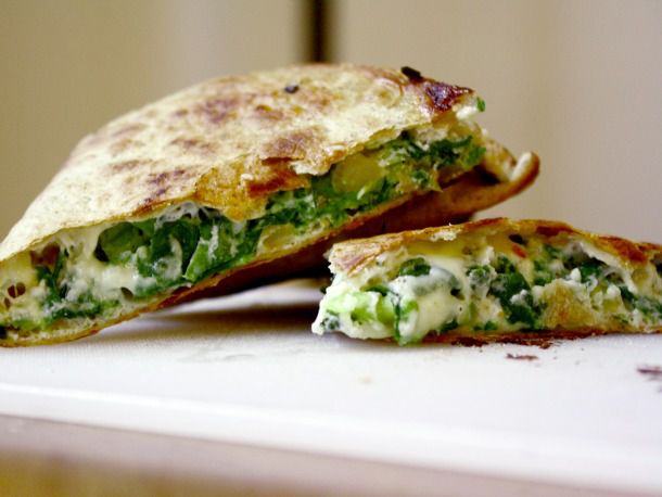 Side view of a spinach pie quesadilla, sliced into wedges and arranged on a cutting board.