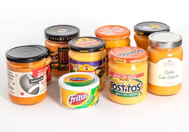 A group of nine queso dips in jars against a white background.