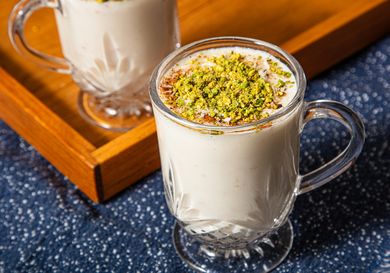 Two glasses of sahlab topped with pistachios and spices on a tray