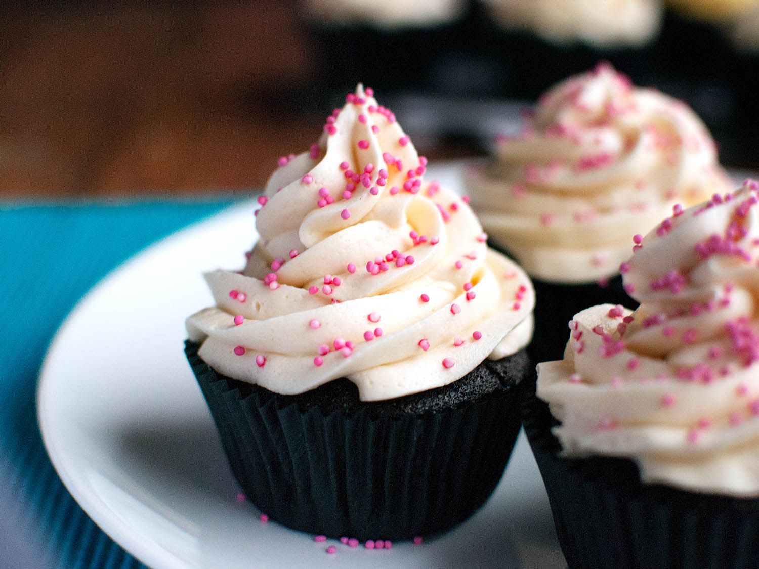Three flour buttercream cupcakes on a plate with pink sprinkles.