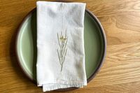 A cloth napkin with a floral embroidery on a green plate, placed on a wooden table