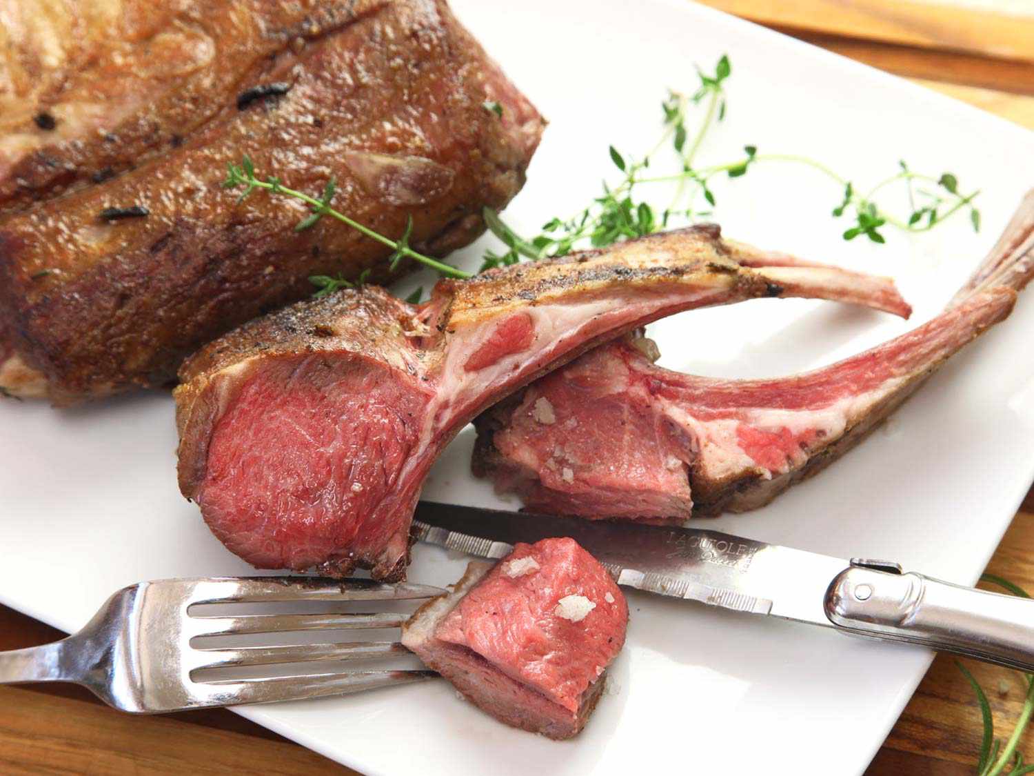 Sous vide lamb ribs on a white plate, next to a fork and carving knife