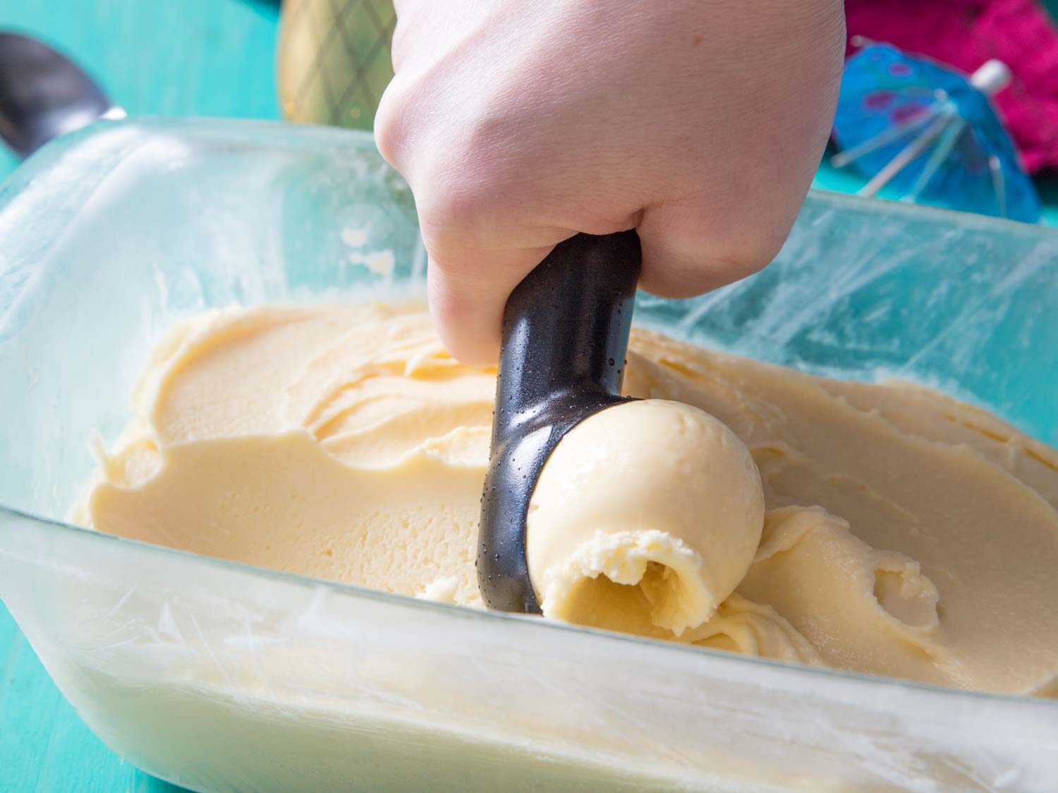 scooping pineapple ice cream from a glass loaf pan