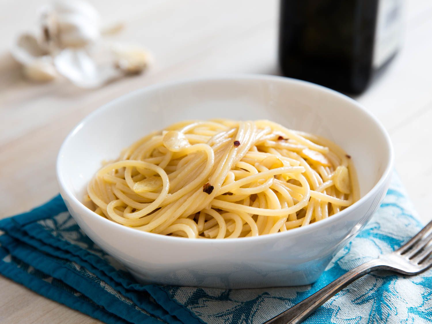 a bowl of aglio e olio pasta flanked by garlic cloves and a bottle of olive oil in the background