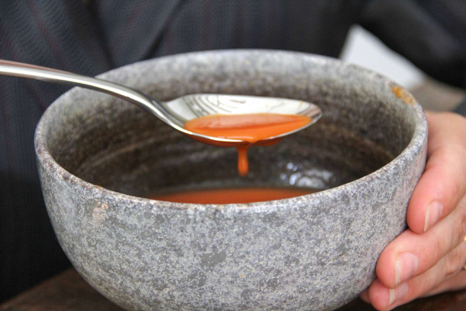 A person scooping soup out of bowl using a spoon from the Robert Welch Caesna Mirror 5-Piece Flatware Place Setting 
