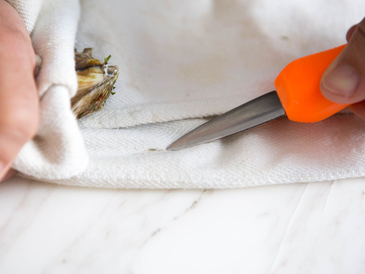 The blade of the oyster knife is brushed against the kitchen towel to remove shell fragments.