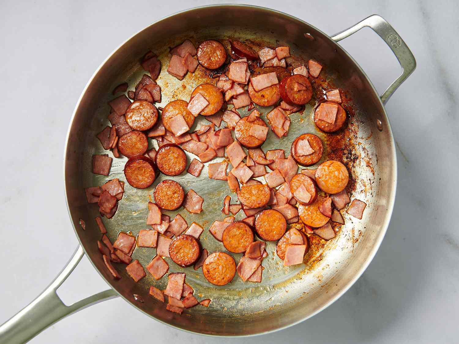 Lightly browned ham and sausage in a large stainless steel pan.