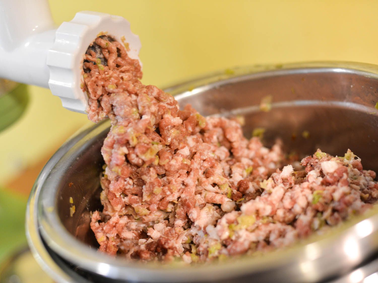 Meat, fatback, and leeks are run through the large plate of a KitchenAid food grinding attachment.