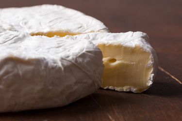 A wheel of brie cheese with a slice cut and slightly pulled away to show the creamy interior.