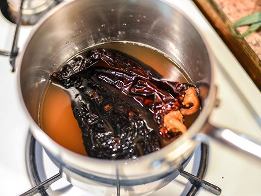 Whole chiles simmering in a saucepan with chicken stock.