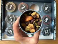 A person holding a tin of trail mix over an Advent calendar