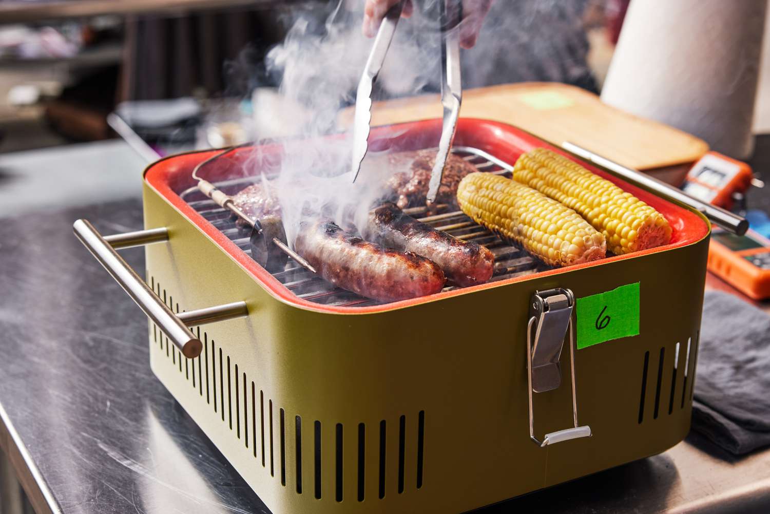 Closeup of brats, burgers, and corn cooking on the Everdure Cube Portable Charcoal Grill