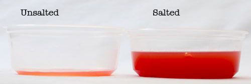 Two half-pint deli containers containing liquid drained from gazpacho vegetables. The one on the left, labeled "unsalted," has enough drained liquid in it to cover the bottom, but little more. The deli container on the right, labeled "salted," is over half-full.