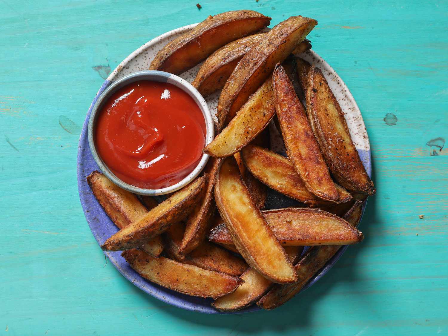 A serving plate of roasted potato wedges with a ramekin of ketchup.