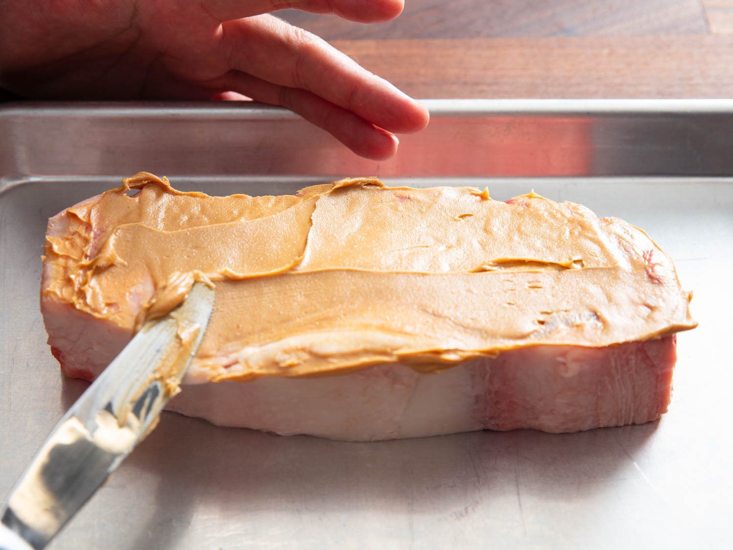 Spreading peanut butter on a raw steak with a table knife. 