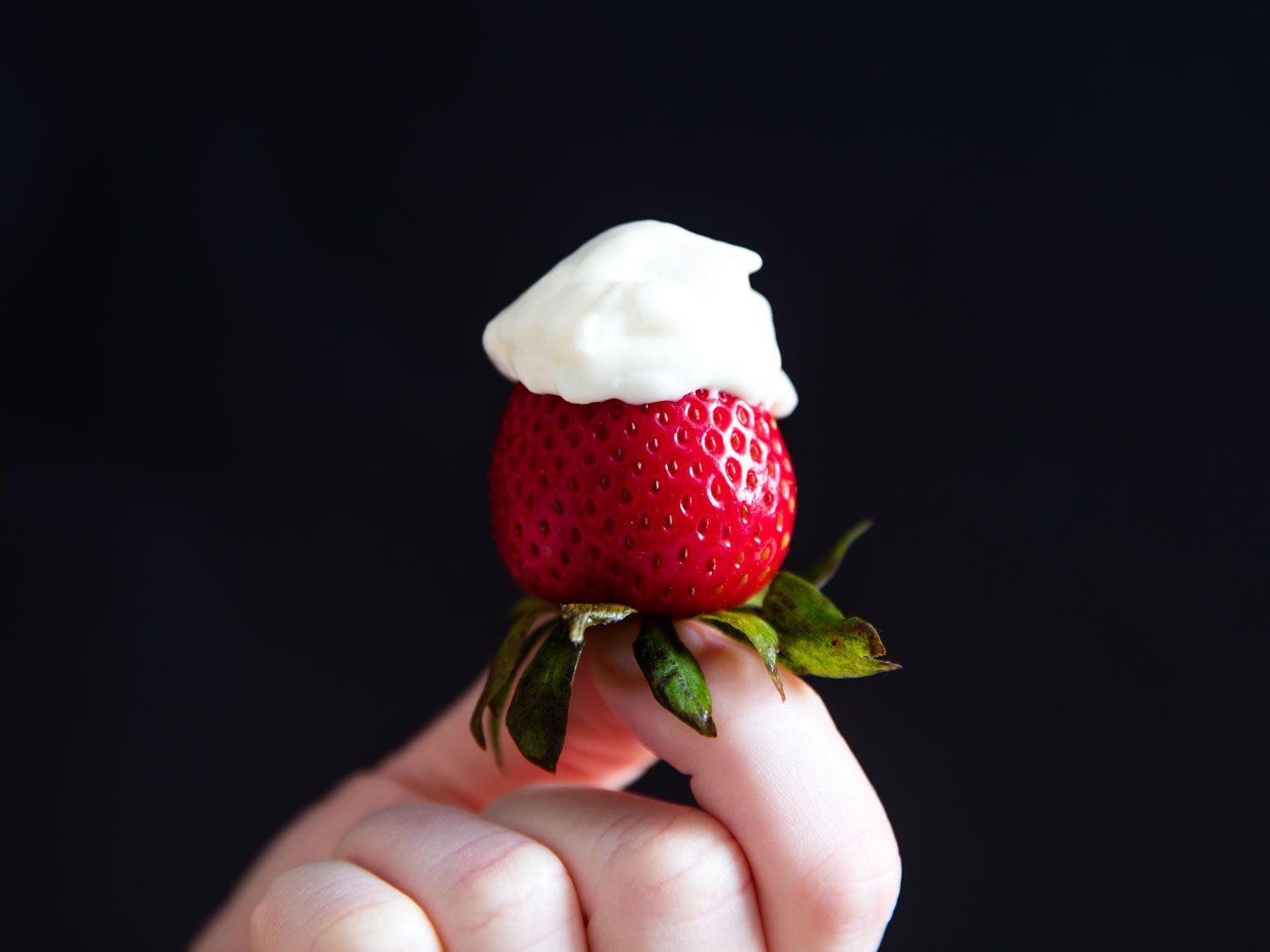 A single fresh strawberry, its peaked dipped in diy cool whip. 