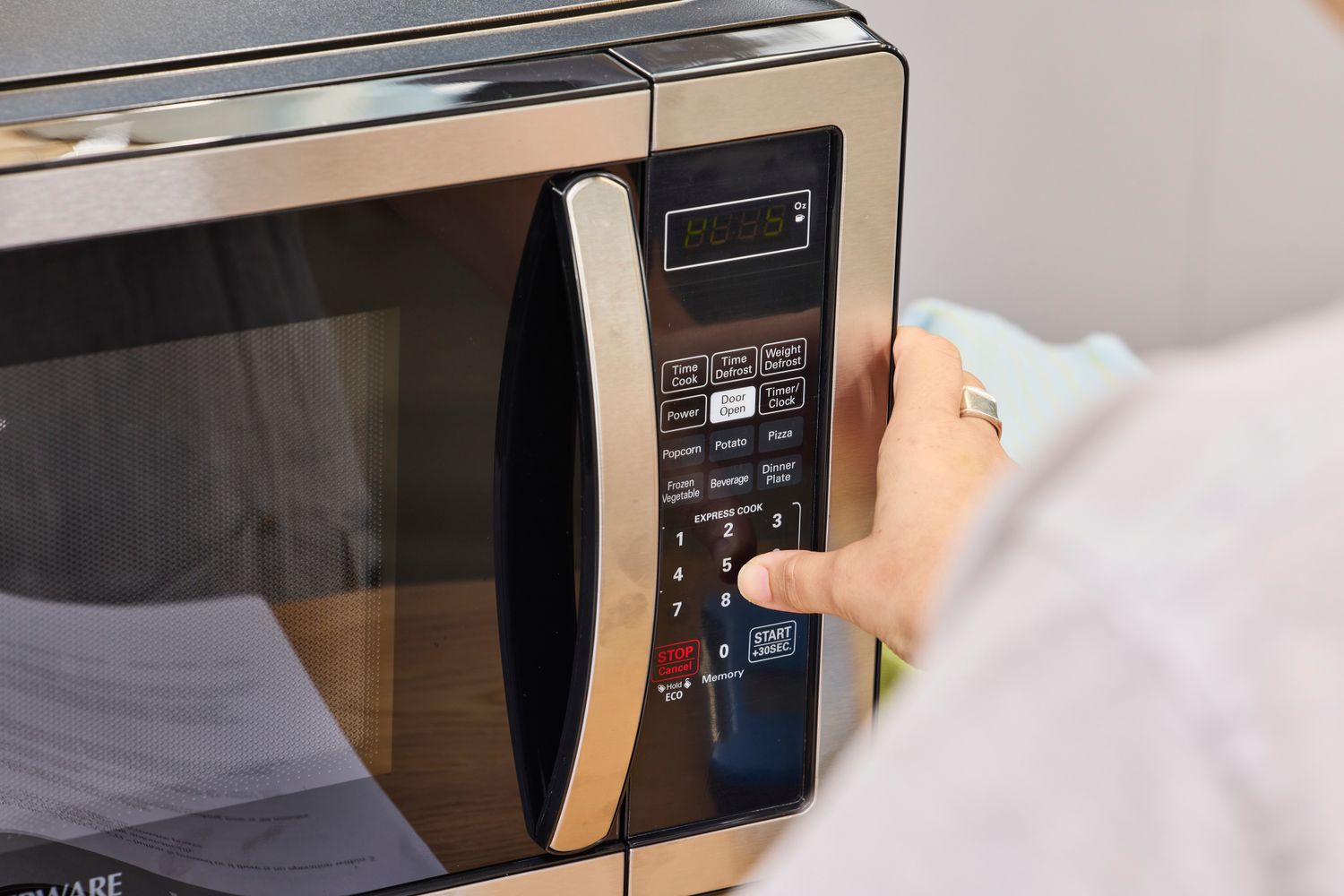 A thumb pressing a button on the Farberware Countertop Compact Microwave (FMWO11AHTBKB) 