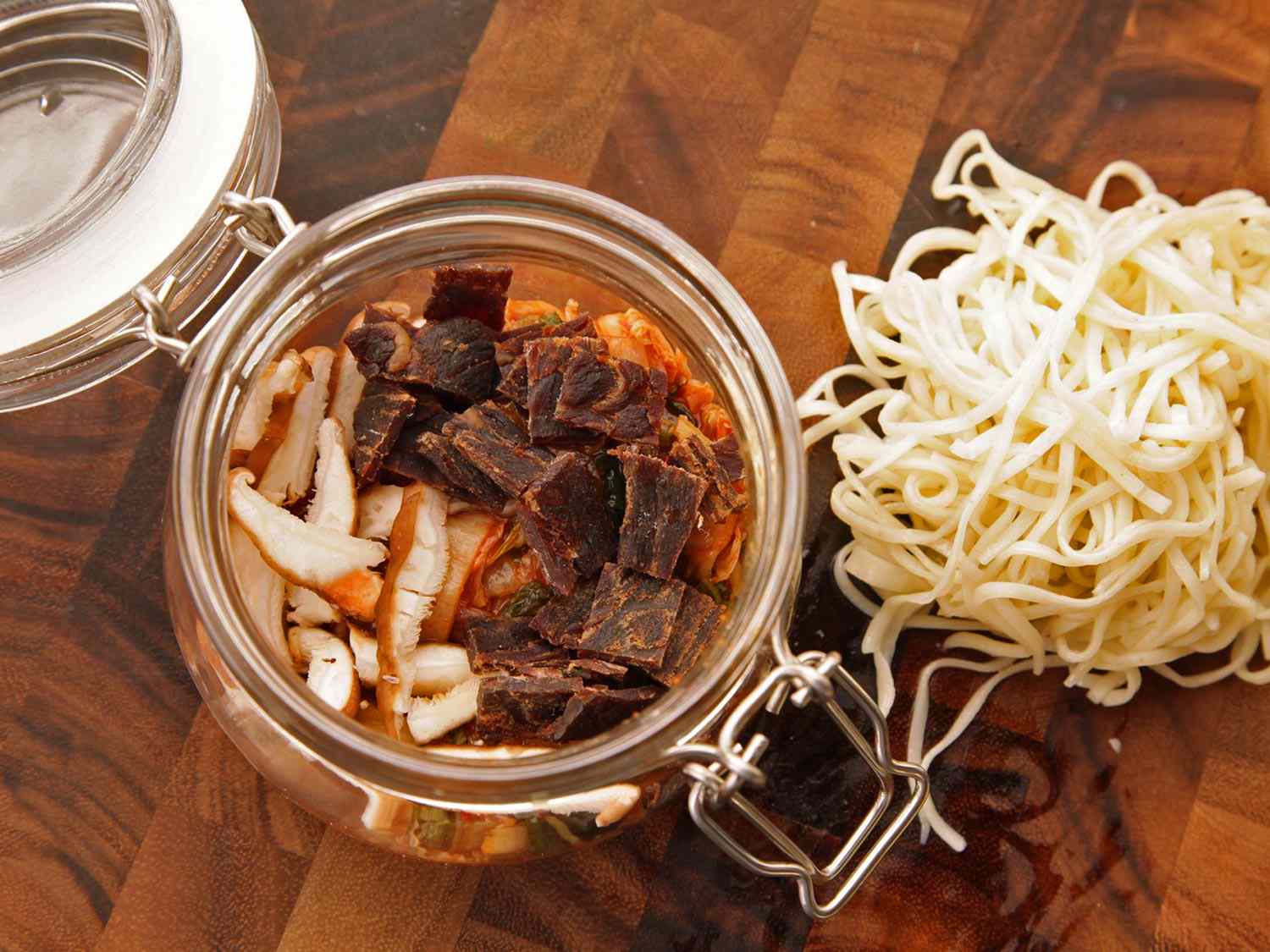Overhead closeup of the jar with flavorings and a pile of par-cooked noodles nearby.
