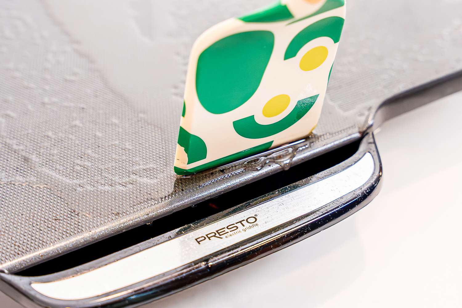 A spatula. guiding bacon grease into an electric griddle's trench