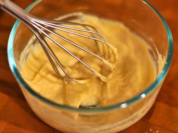 A prep bowl of mustard. A mini whisk resting on the edge of the bowl.