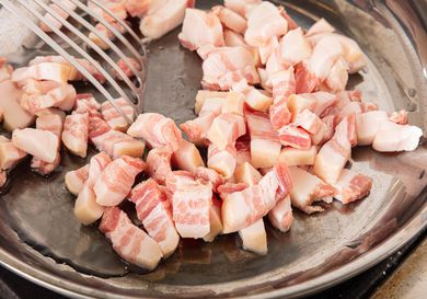 Diced pancetta in a skillet being stirred with a slotted spatula