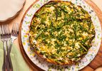 Smashed potato tart with asparagus and herbs on a floral plate, placed on a wooden table with forks and a green napkin nearby.
